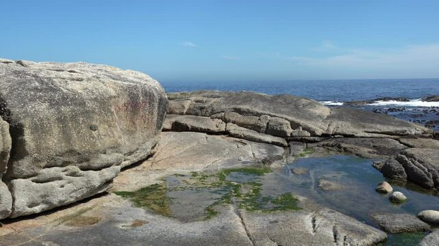 Big granite beach rocks along a rocky shore with seaweed in the sea