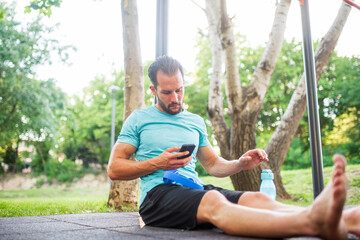 Naklejka premium Athletic man using smartphone at outdoor gym