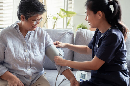 Young Asian woman nurse take care senior woman at nursing home, checking blood pressure for observe health condition. Healthy senior home care or medical concept.