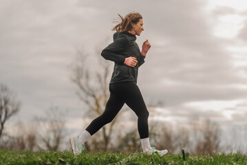 Young sporty woman running in a park during a cloudy day