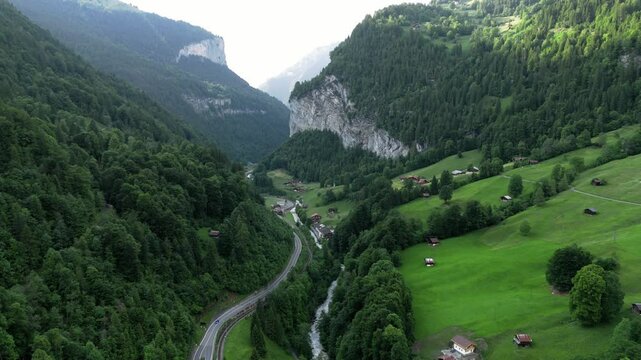 Flyinge over the beutiful forresty and mountainous alp valley of grindelwald Switzerland near Lauterbrunnen with its creek Weisse L&uuml;tschine during summer time
