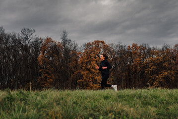 Woman running in a meadow by the forest on a cloudy autumn day