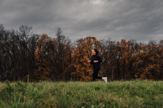 Woman running in a meadow by the forest on a cloudy autumn day