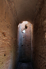 Ancient narrow brick corridor with arched ceiling and holes in the walls, showing historical architecture