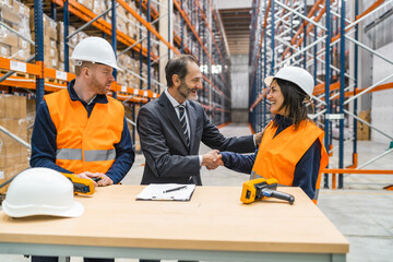 Manager shaking hands with a woman warehouse worker while finalizing a deal in a logistics center, with her colleague standing next to her