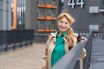 Portrait of a laughing 60-year-old Caucasian woman with long red hair in a ponytail. A woman wearing a neutral-colored raincoat and a green blouse.