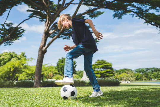 Little boy playing football in the garden with morning sunrise
