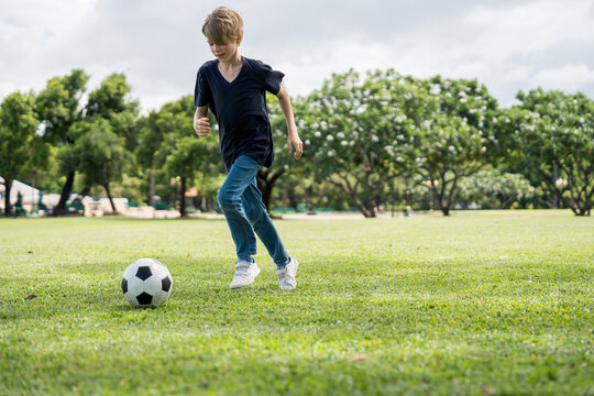 Little boy playing football in the garden with morning sunrise