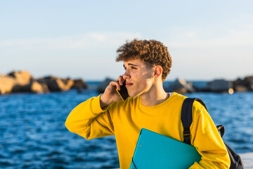 College student talking on smartphone by the sea holding a binder