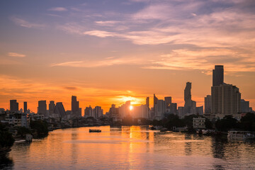 Sunrise over Chao Phraya River in Bangkok with golden skyline tall buildings reflecting in water.
