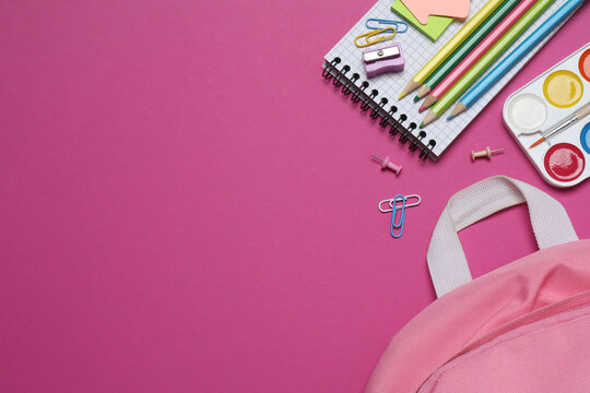 A pink backpack with colorful school supplies on a color background. Top view, space for text