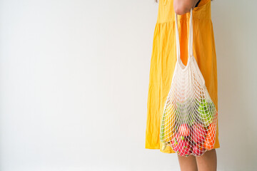 Woman holding mesh shopping bag with organic apple, corn, carrot, dragon fruit and lettuce on white background. Reusable shopping bag. Zero waste. Plastic free. Eco friendly concept.
