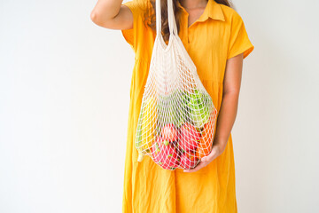 Woman holding mesh shopping bag with organic apple, corn, carrot, dragon fruit and lettuce on white background. Reusable shopping bag. Zero waste. Plastic free. Eco friendly concept.