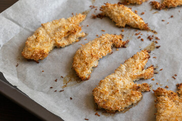  baked chicken fillets coated with coconut shreds on a tray. Tropical flavor dish, crispy texture, rich taste — perfect meal for dinner