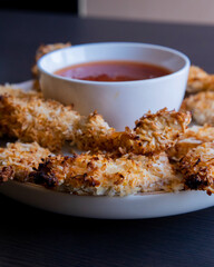  chicken fillets coated with coconut shreds, placed on a plate with sweet chili sauce. Tropical flavor dish, crispy texture, rich taste 