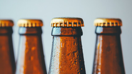 Cold brown glass beer bottle with golden cap and water droplets on plain background