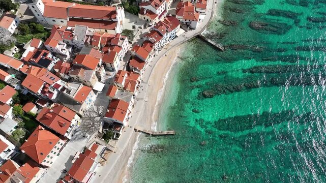 Baska beach and coastline with crystal-clear turquoise water, marina boats, city street, sunny summer mood captured from drone view on Krk Island. Baska vacations town in Adriatic sea