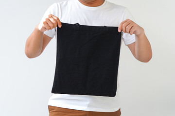 Young man hand holding black canvas tote bag on white background. Reusable eco bag for shopping. Eco friendly concept. Mockup for you designs.