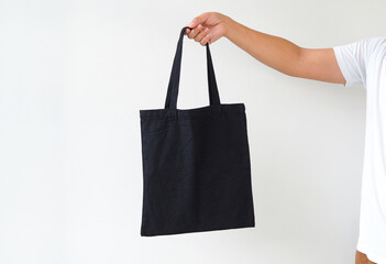 Young man hand holding black canvas tote bag on white background. Reusable eco bag for shopping. Eco friendly concept. Mockup for you designs.