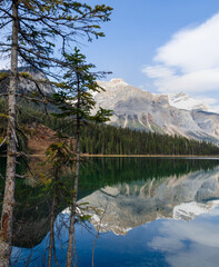 Panoramic view of Emerald Lake in Yoho National Park with pine trees and snow-capped mountain with reflected in calm water in Alberta, Canada
