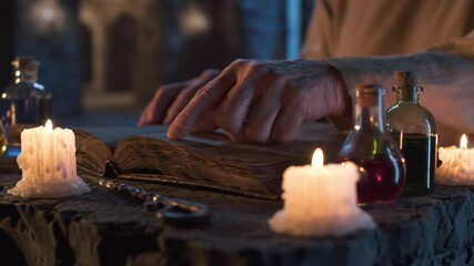 Finger sliding gently over aged book pages as flickering candles and glass vials filled with mysterious liquids decorate medieval stone setting, creating rich fantasy atmosphere.