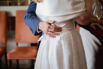 Close up of a grooms hand hugging the bride in white dress, back view