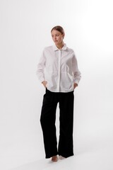 Model poses elegantly in a minimalist studio wearing a white shirt and black trousers while showcasing modern fashion trends