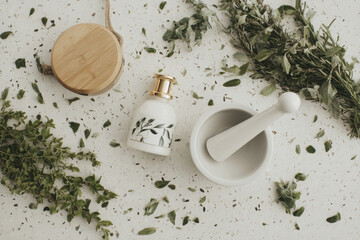 Stylish arrangement of mortar and pestle, decorative bottle, and fresh herbs on speckled surface creates serene kitchen atmosphere. This evokes sense of natural cooking and wellness