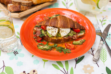 Homemade croissant sandwich with avocado, poached egg, bacon, arugula, and cherry tomatoes. A stylish brunch with a child enjoying the meal