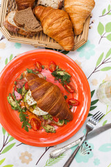 Homemade croissant sandwich with avocado, poached egg, bacon, arugula, and cherry tomatoes. A stylish brunch with a child enjoying the meal