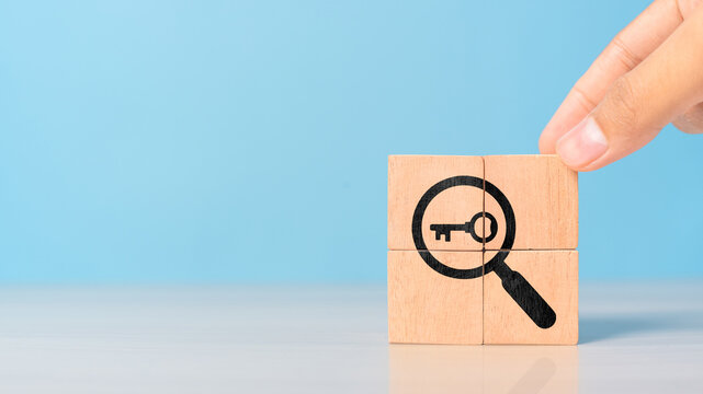 Hand holding wooden cubes with magnifying glass and key symbols. Represents business problem-solving, strategy, and innovation for effective decision-making.