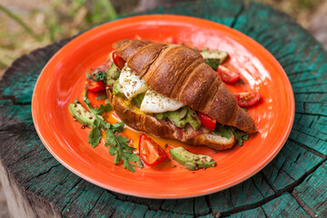 Homemade croissant sandwich with avocado, poached egg, bacon, arugula, and cherry tomatoes. A stylish brunch with a child enjoying the meal