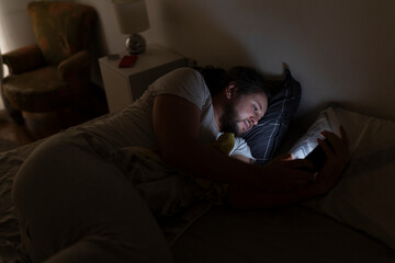 Man lying in bed at night using smartphone in dark room