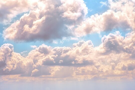 Dynamic and dramatic skyward view of an intricate cloudscape. Sunlight brilliantly bursts through breaks in the voluminous, dark grey and white clouds, creating striking crepuscular rays that fan acro
