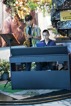 Young man playing saxophone and  piano smiling at a restaurant table