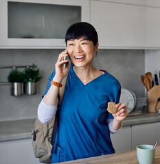 Portrait of a young asian nurse woman gettyng ready for work drinking a glass of water for hydration and talking on a mobile phone smartphone  standing in kitchen home. Overworked, busy, stress, urgen