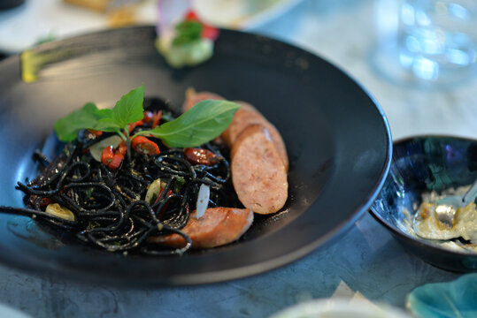 Black spaghetti with sausage  beautifully presented with gourmet food on a decorated table in a restaurant setting 