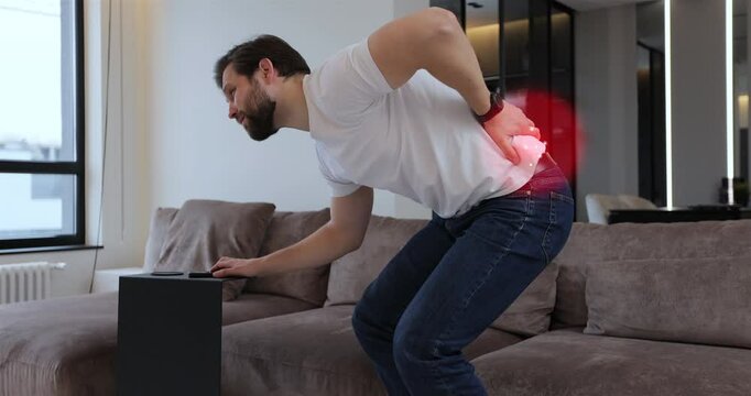 Young bearded man with spinal problems bends over with back pain at home, digital 3d animation with red pulsating sore zone of problem area.
