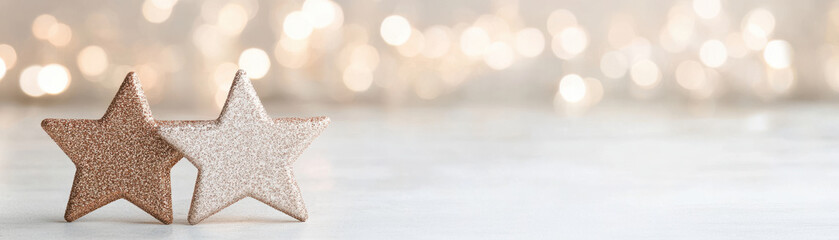 Two glittery star shaped ornaments in warm golden tones with soft bokeh lights creating festive and cozy atmosphere