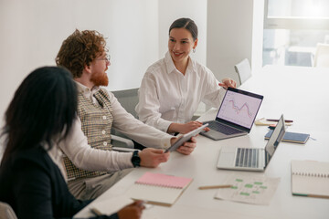 A team collaborates in a modern workplace, analyzing data on laptops and tablets during their meeting