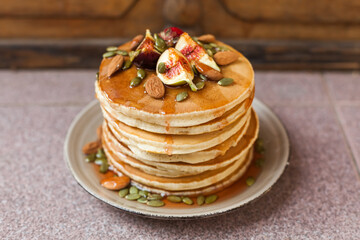 Stack of pancakes with fresh fig, strawberries, maple syrup, and crunchy toppings. A warm,...