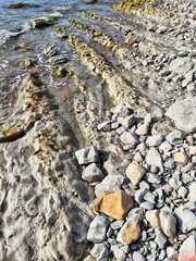 coastwhere the water meets the rocky shore. a shore of layered rock formations and pebbles. an unusual rocky shore