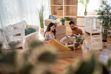 Young couple unpacking boxes and assembling furniture in new home