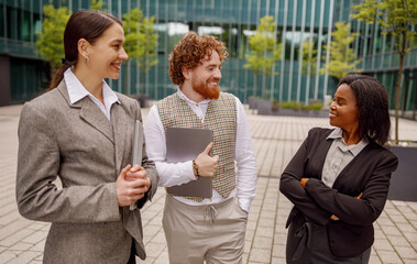 Three professionals, engaged in a casual yet productive meeting outdoors, collaborate in a modern corporate setting
