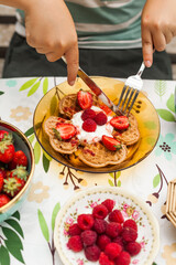 Heart-shaped waffles topped with berries and whipped cream. A cheerful brunch moment with a child enjoying the treat