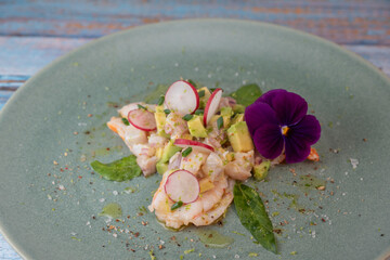 Delightful ceviche made with fresh dorade and shrimp, complemented by avocado and radish, garnished with an edible flower on a serene green plate.