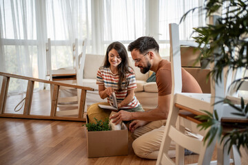 Young couple unpacking boxes and assembling furniture in new home