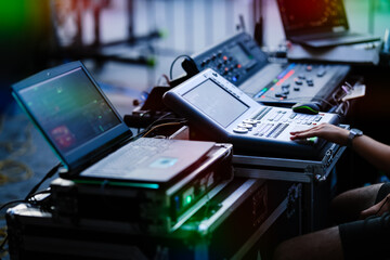Close-up of a stage technician operating a digital control console and laptop during a live event. Professional audiovisual setup with lighting or sound control equipment.