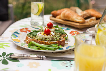 Rustic avocado toasts on oval bread served for a cozy family brunch with orange juice, croissants,...