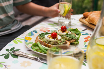 Rustic avocado toasts on oval bread served for a cozy family brunch with orange juice, croissants,...